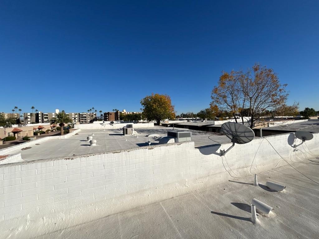 Before photo of a weathered foam roof on a Mesa multifamily building, showing chalked coating, rooftop equipment, and satellite dishes