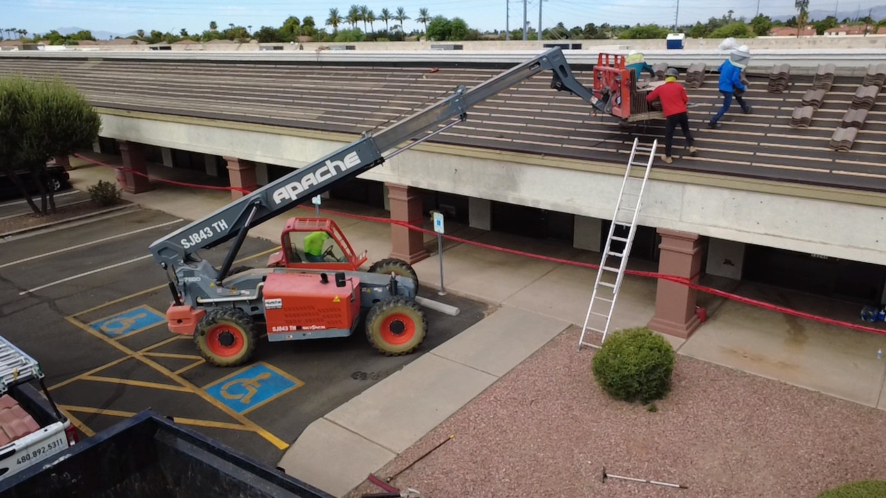 CS13 5 Progress photo of new concrete tile being roof-loaded onto a stripped and battened commercial mansard roof by a telehandler boom lift