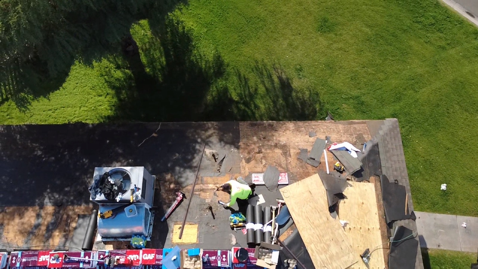 CS14 5 Overhead progress photo of the shop roof stripped to the deck, with a new sheet of CDX plywood installed, felt underlayment going down, and GAF Timberline shingle bundles staged along the eave