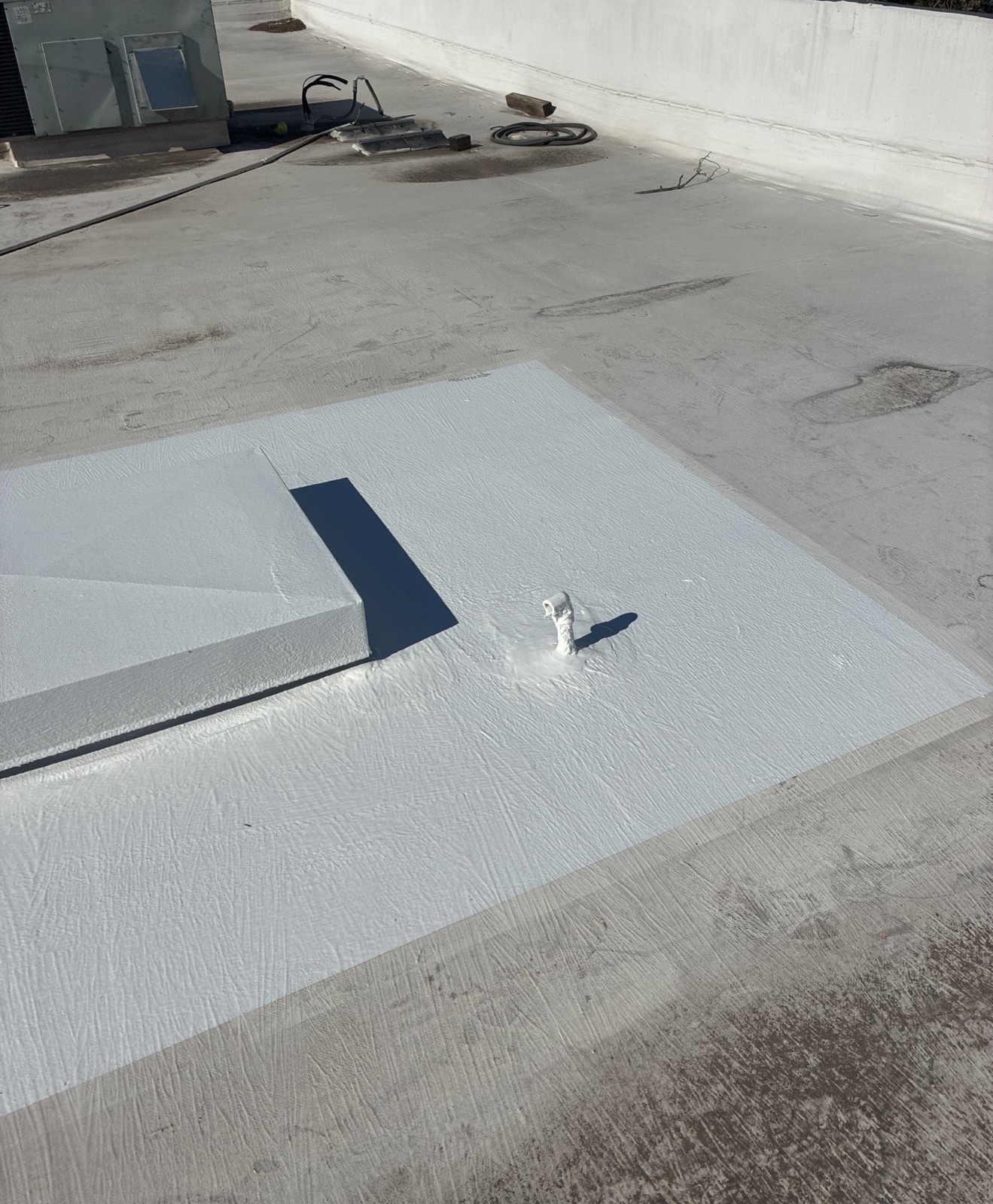 After photo of a completed silicone repair area on the TPO roof, with a coated curb and a sealed pipe penetration surrounded by untouched membrane