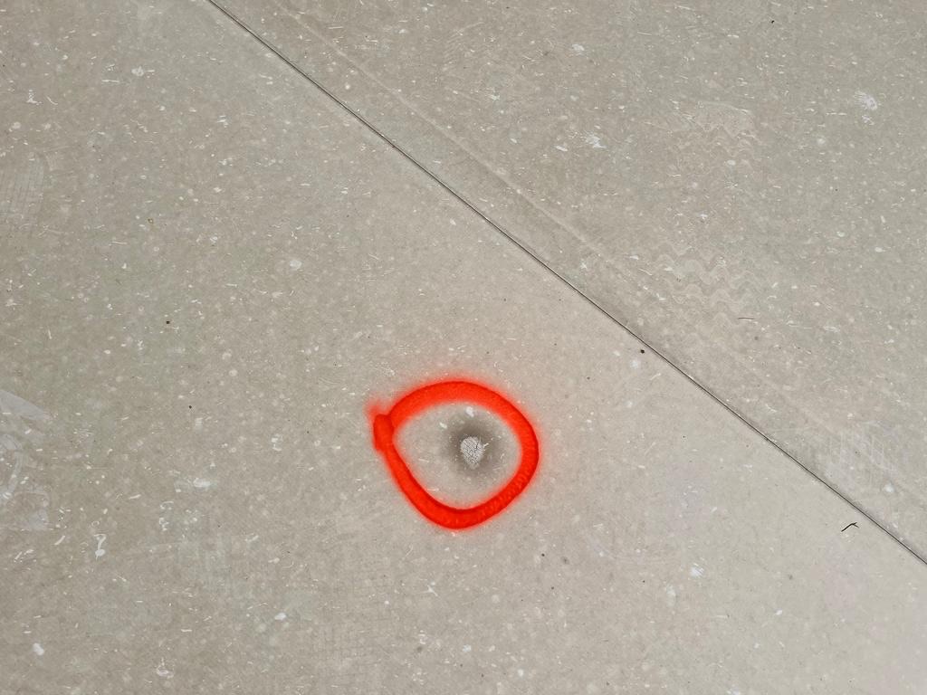 Before photo of a puncture through a commercial TPO single-ply roof membrane, circled with inspection marking paint beside a heat-welded lap seam