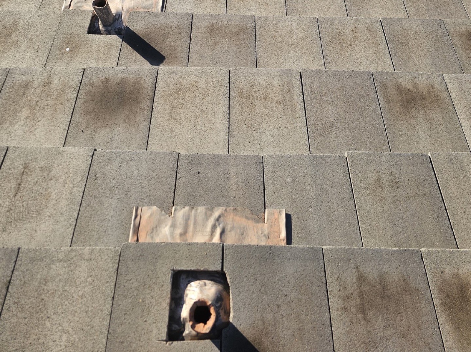 CS16 1 Before photo of a Tempe concrete tile roof with underlayment lifted and torn open around two pipe penetrations