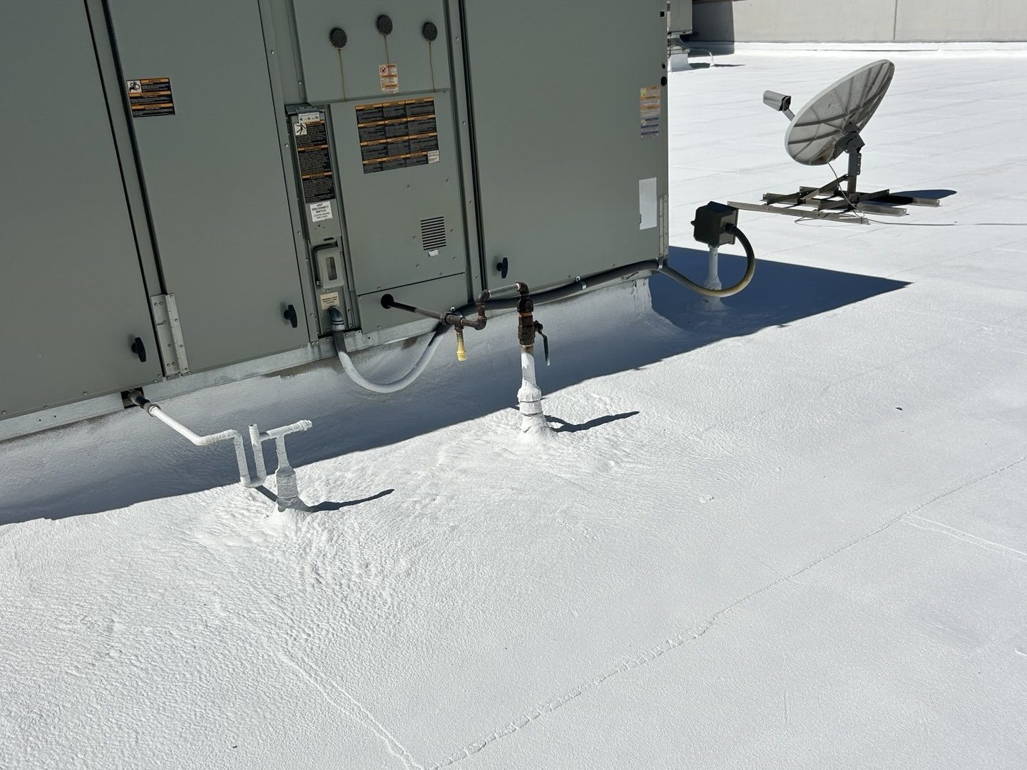 After photo of the restored Phoenix cap sheet roof with a white acrylic coating and newly detailed pipe penetrations beside a rooftop air handling unit