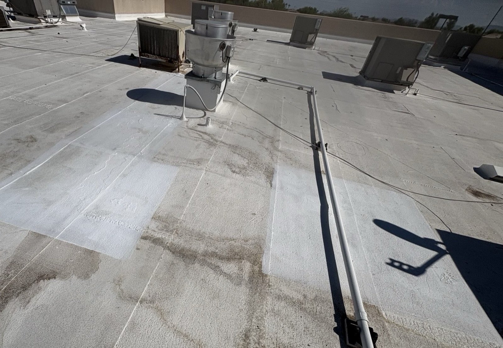 CS19 7 After photo of the Gilbert commercial roof field with a freshly recoated section covering the former runoff track, with rooftop equipment and conduit in the background