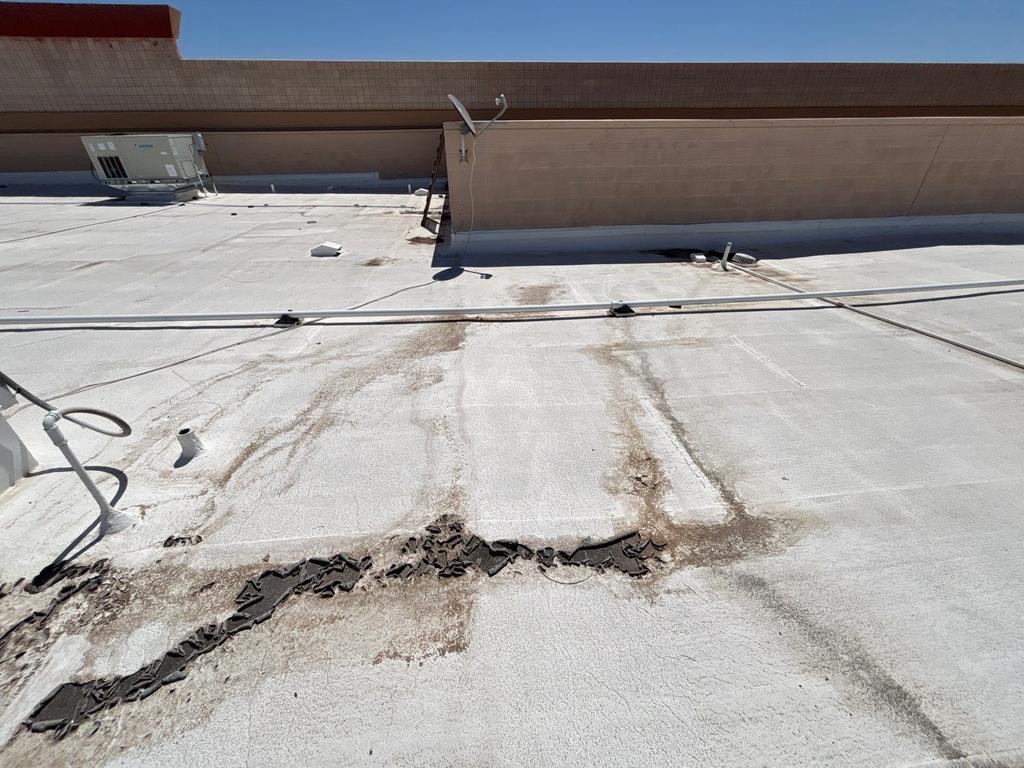 CS19 6 Before photo of a Gilbert commercial roof field showing runoff staining streaks, coating peeled loose along a seam, and debris, with rooftop equipment and a parapet wall behind