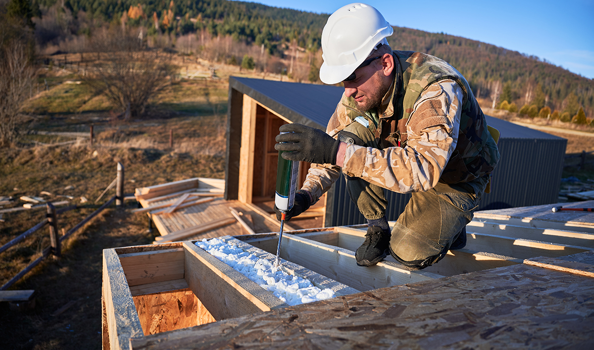 Male Builder Doing Thermal Insulation On Roof Of Wooden Frame House By Polyurethane Foam