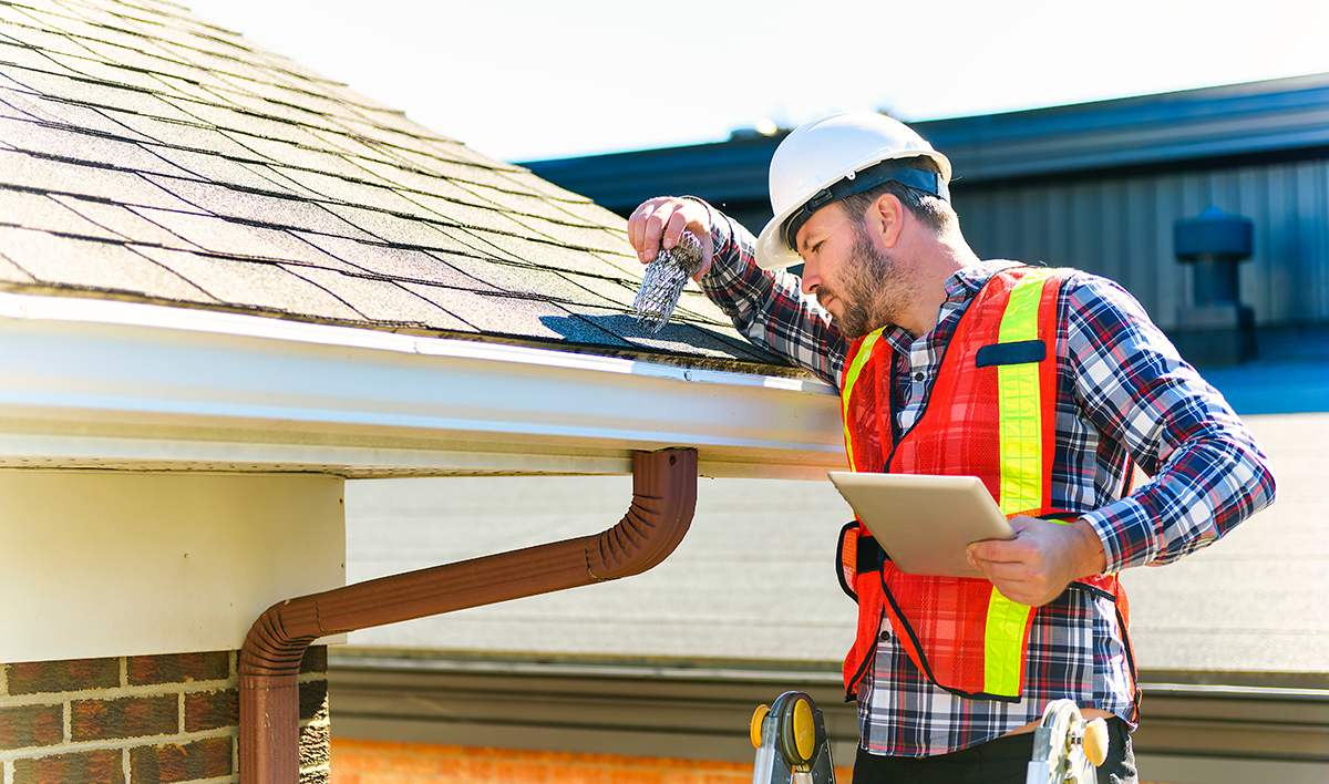 Man With Hard Hat Standing On Steps Inspecting House Roof