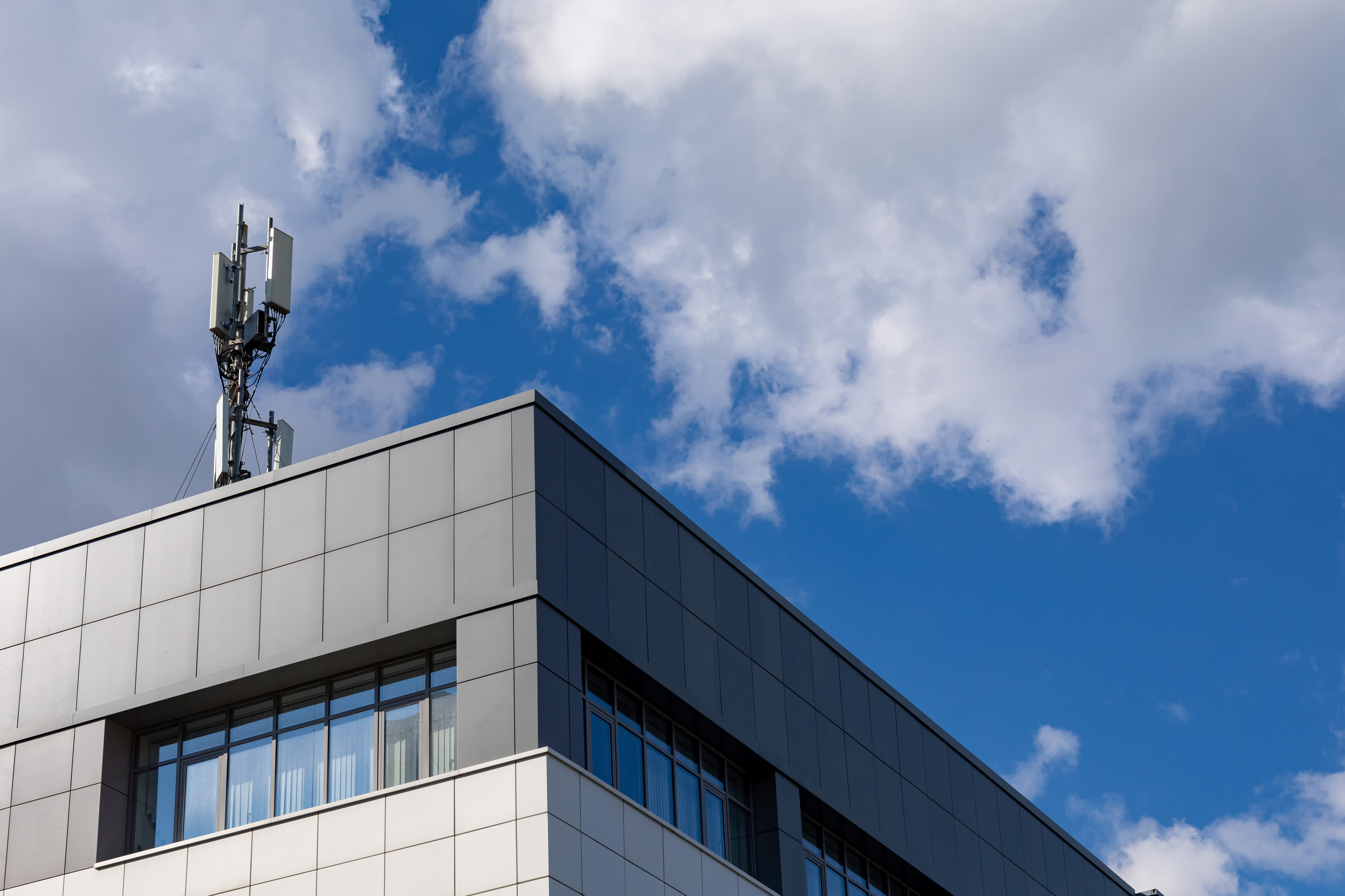 4G, 5G Transmitters In An Urban Environment Cellular Base Station With Transmitting Antennas On The Roof Of An Office Building Against A Cloudy Sky